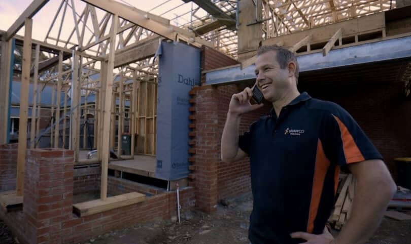 A builder smiling and talking on the phone at a job site