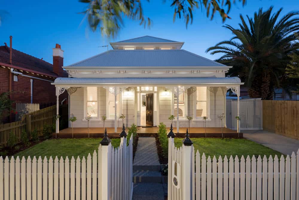 A completed white house with a white picket fence and freshly mowed garden