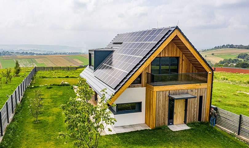 A wood house covered in solar panels in a green country field