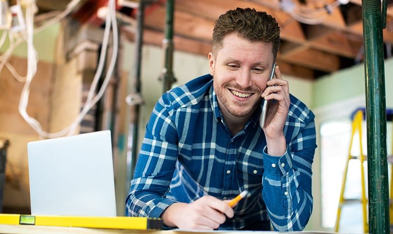 A builder talking on the phone on-site with a laptop near by