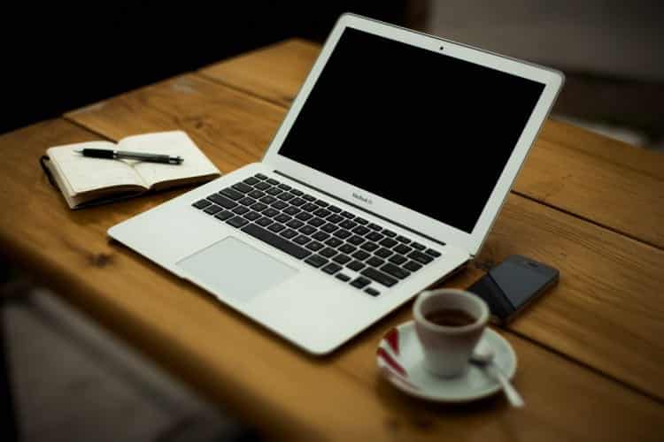 A laptop on a brown desk with a cup of coffee