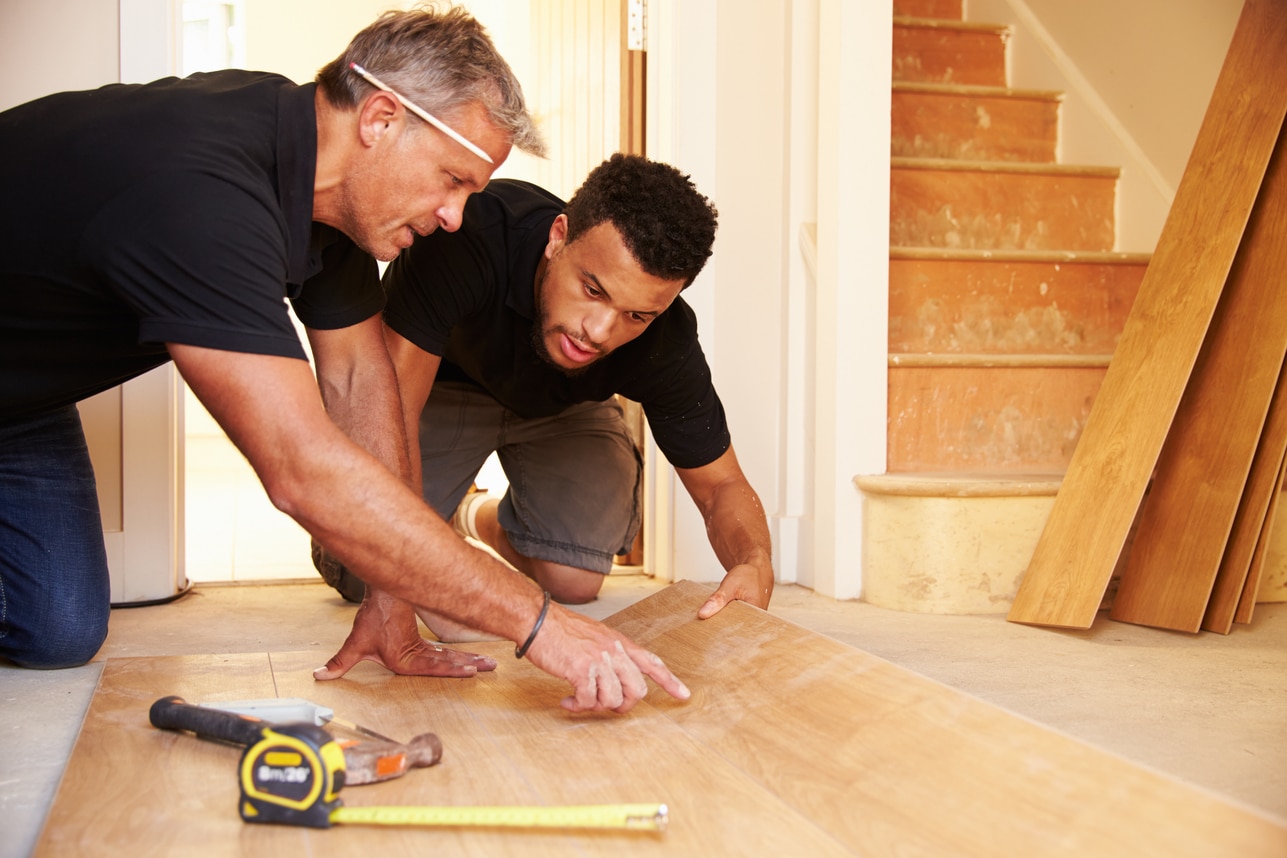 two tradies install flooring in a house