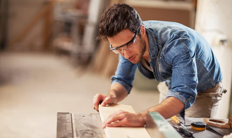 A carpenter measuring up a piece of wood with protective gear on