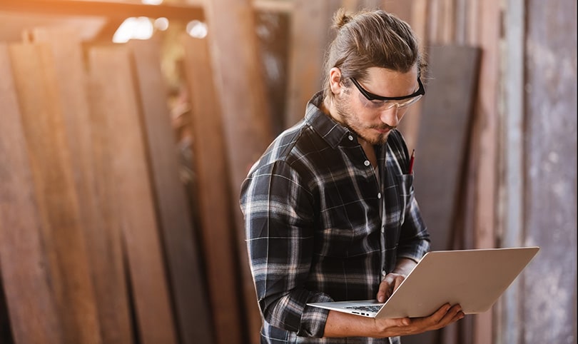 A young carpenter using a laptop in a workshop