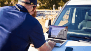 Residential builder reviewing construction drawings on a laptop while preparing a construction takeoff at a job site