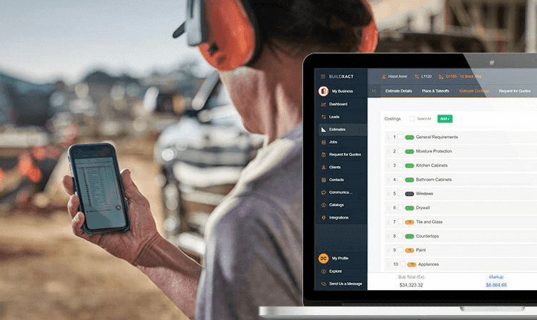 Construction professional on a job site reviewing project costings on a smartphone while a laptop displays the Buildxact estimating and job costing interface.