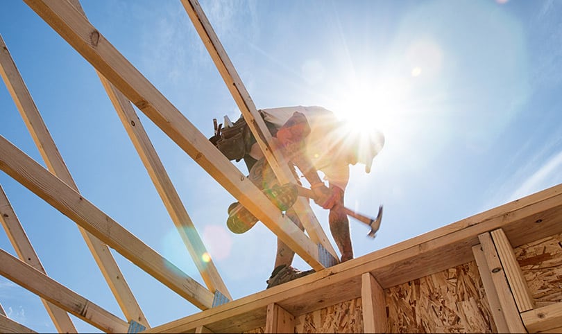 A builder working on a roof under the sun and blue sky