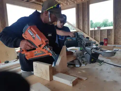 Two builders working on timber with a nail gun and a saw