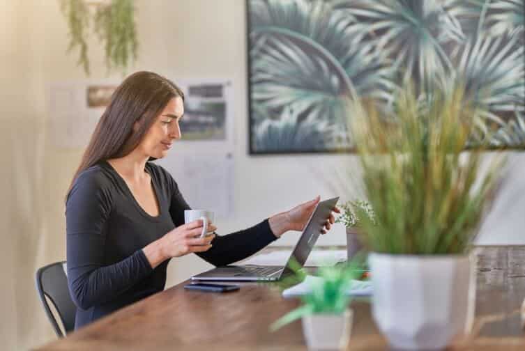 A woman using a laptop and drinking out of a mug