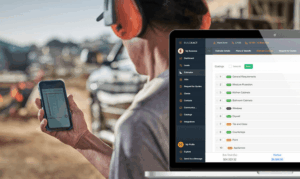 Contractor reviewing a preliminary construction estimate on a mobile phone while cost breakdowns are displayed in estimating software on a laptop at a job site.