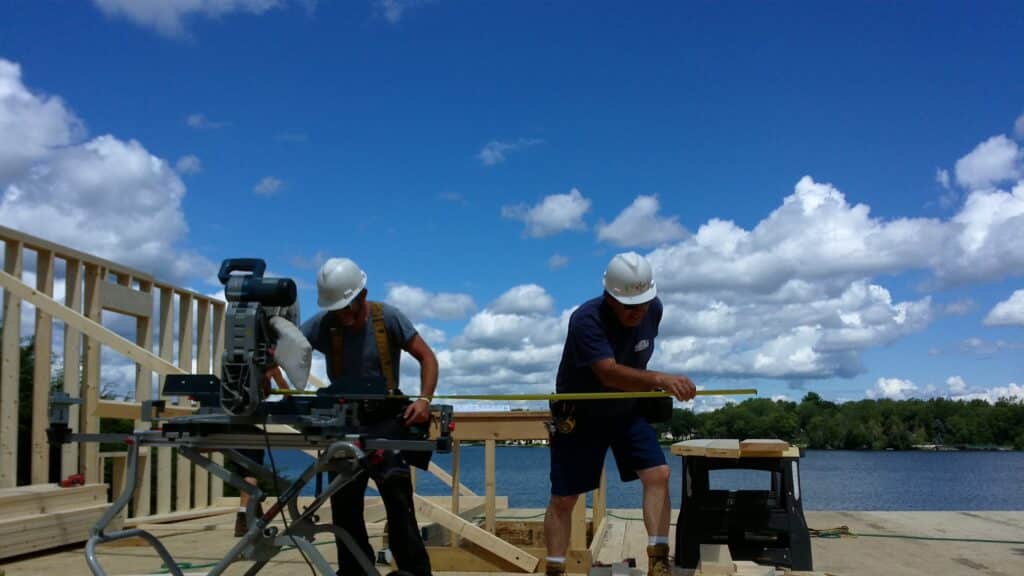 Two builders working on timber on-site underneath the blue sky