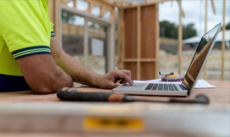 A builder uses his laptop while working at a home construction job site.