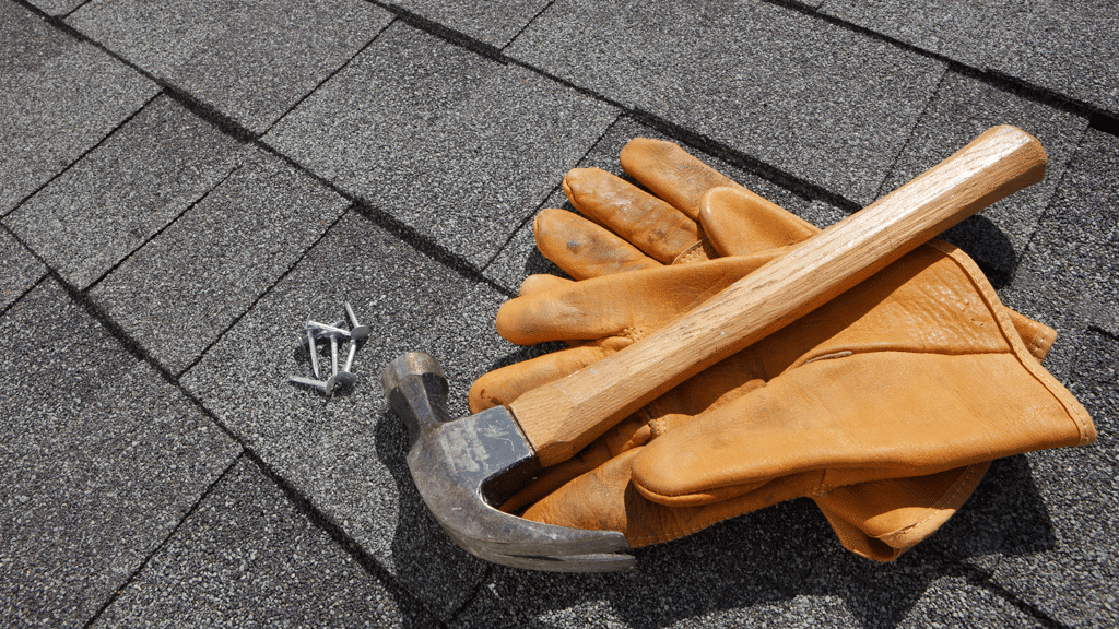 a roofing contractor's gloves, hammer and nails lie on top of installed roofing tiles.