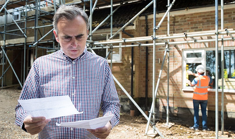 A site manager looking over paperwork on-site with a builder in the background