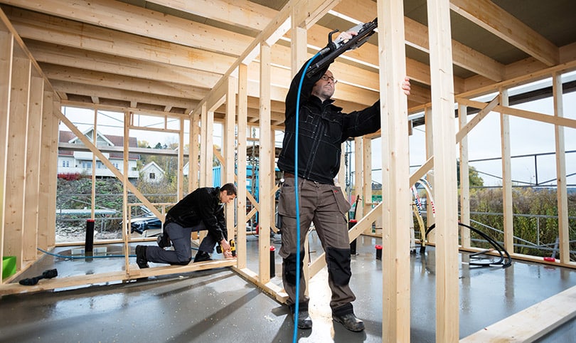 Two builders using nail guns to put up framing on a job site