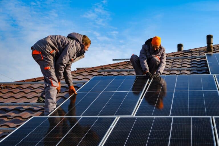 Two builders installing solar panels onto a roof