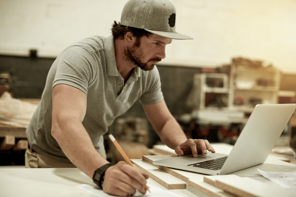 A builder works on a laptop while making notes