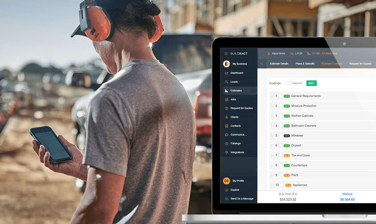 A residential builder on a construction site checks his phone while a laptop displays the Buildxact estimating interface with line items for kitchen cabinets, bathroom cabinets, windows, drywall, and other costings.