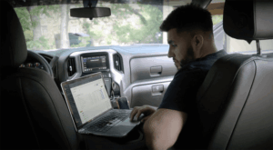 Residential builder reviewing estimate and job costs on a laptop from a truck at the jobsite.