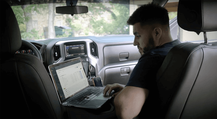 Residential builder reviewing estimate and job costs on a laptop from a truck at the jobsite.