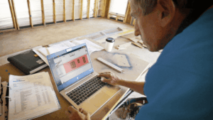 Contractor reviewing digital construction drawings and documents on a laptop at a residential job site before starting work.